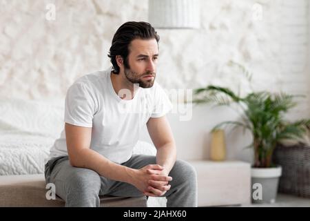 Upset guy in pajamas sitting on bed at home Stock Photo