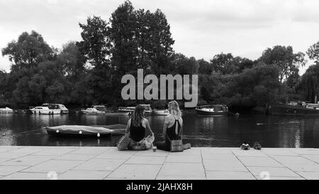 Richmond, Greater London, England, May 18 2022: Friends chat on the riverbank at Richmond Upon Thames with boats moored. Stock Photo