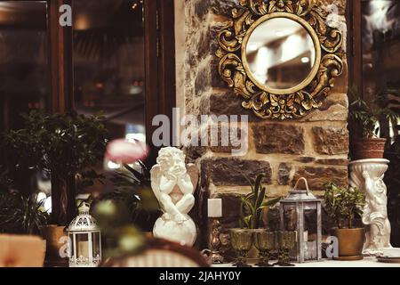 Russia, Sochi 02.10.2021. A gold framed round mirror hangs on a stone wall by the windowsill with angels, lanterns and other decorative vintage luxury Stock Photo