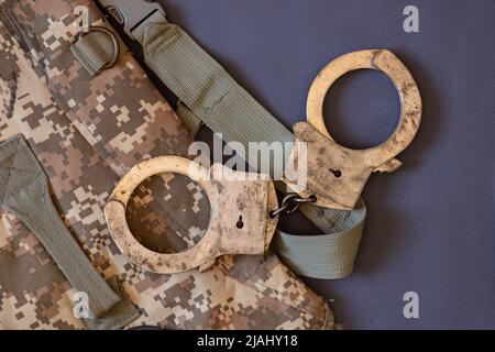 Old handcuffs lie on a camouflage bag , law and justice Stock Photo
