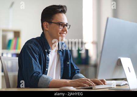 Portrait Of Smiling Young Male Office Employee Working On Laptop Stock Photo
