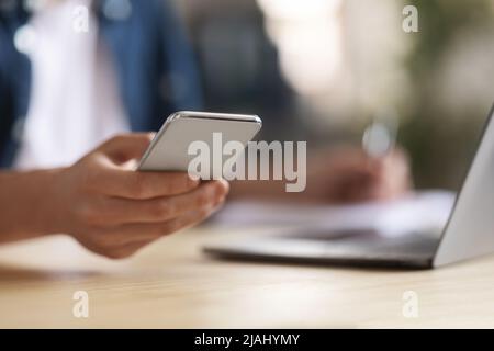 Young Male Using Modern Smartphone While Sitting At Desk With Laptop Stock Photo