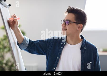 Smiling young male entrepreneur writing notes on white board in office Stock Photo