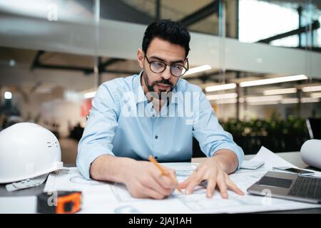 Serious concentrated young middle eastern man professional engineer with beard working with project drawings Stock Photo