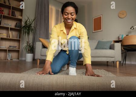 African Woman Covering Floor With Carpet Decorating Room At Home Stock Photo