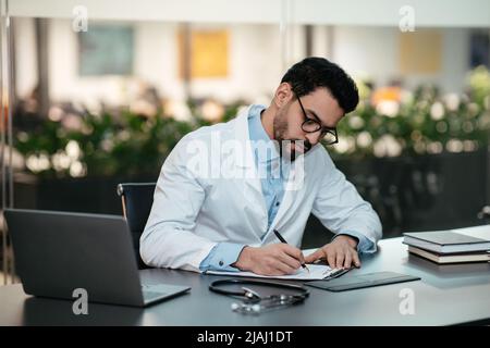 Serious busy concentrated handsome young islamic man doctor with beard in glasses, white coat works in clinic Stock Photo