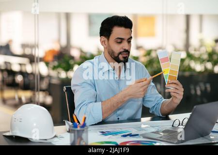 Serious young islamic male engineer designer with beard shows color palettes in laptop in office Stock Photo