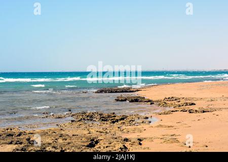 Sandy and rocky beach of the red sea in Egypt South Sinai at the daylight in summer, Natural panoramic empty shore with no people with sea waves hits Stock Photo