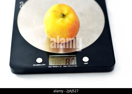 Weighing an Apple fruit on a digital kitchen scale in grams isolated on white background, healthy food, weight loss concept, calculating food calories Stock Photo