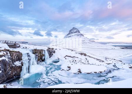 The frozen waterfall of Kirkjufellfoss in Iceland in Winter covered in ice and snow with Kirkjufell mountain in the background Stock Photo
