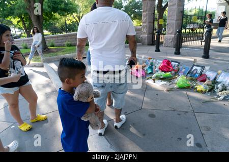 Austin Texas USA, May 30 2022: Little boy hugs a stuffed animal as he and his family look at photographs of many victims of the Uvalde, Texas mass murder at Robb Elementary, along with remembrance candles and bouquets of flowers at a makeshift memorial at the steps to the Texas Capitol grounds. Credit: Bob Daemmrich/Alamy Live News Stock Photo