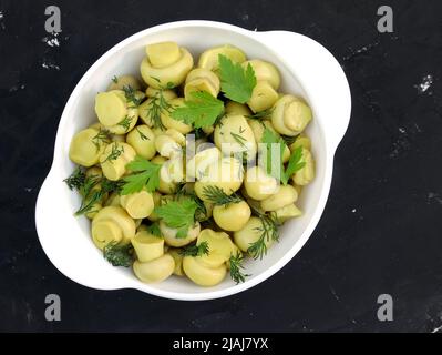 Pickled champignons in a white plate top view. Mushrooms with parsley in a bowl on a black background. Stock Photo