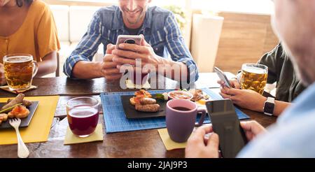 Group of young friends with phones smiling in a cafe bar. Having breakfast and watching mobile. Stock Photo