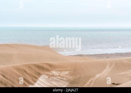 Sand blown from a large dune by the wind with the horizon in the sea behind it. Stock Photo