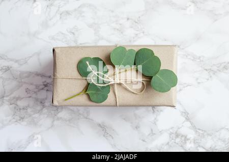 Gift box wrapped in brown paper decorated with eucalyptus branch, natural eco friendly zero waste gift wrapping idea. Top view. Stock Photo