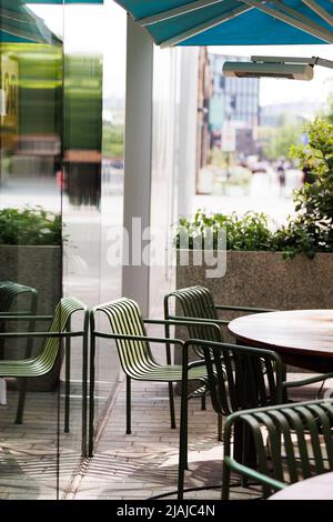 Green chairs around a wooden table for outdoor eating set up in a modern street cafe/ restaurant Stock Photo