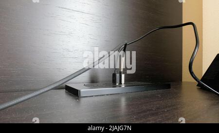 USB charger cables plugged into table top for charging smartphones, iPhones, tablets, and portable devices; USB desk charger desktop charging station. Stock Photo