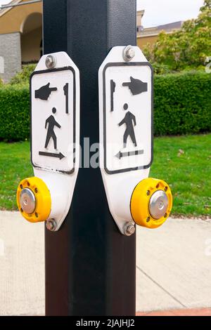Pedestrian crosswalk button on the corner of two streets indicating direction of crossings. Stock Photo