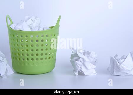 Green trash can. Full basket. Crumpled paper in a basket. A mountain of garbage is scattered on the table. Stock Photo