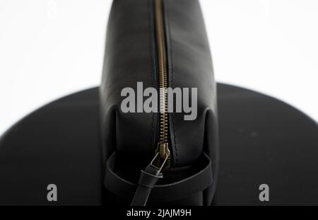 Man's black leather personal cosmetic bag or pouch for toiletry accessory on a black surface with white background. Style, retro, fashion, vintage and Stock Photo