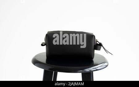 Man's black leather personal cosmetic bag or pouch for toiletry accessory on a black surface with white background. Style, retro, fashion, vintage and Stock Photo
