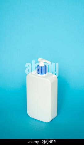 Large white plastic bottle with pump dispenser as a liquid container for gel, lotion, cream, shampoo, bath foam on blue background. Stock Photo