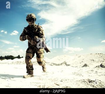 Serviceman running with service rifle in sandy area during military operation. Stock Photo