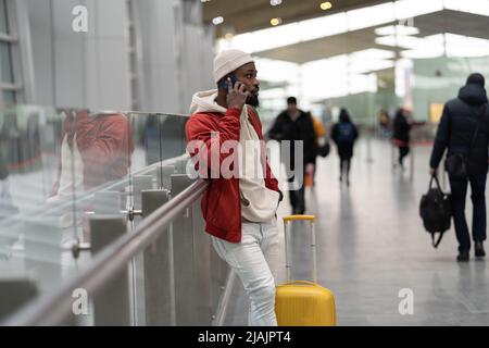 African American young man talking on smartphone travelling with luggage inside in airport terminal  Stock Photo