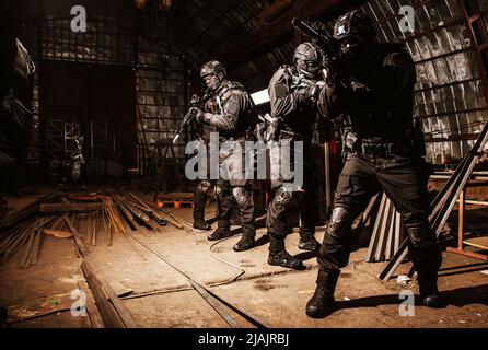 SWAT team armed with sem-automatic rifles moving with caution in an abandoned hangar. Stock Photo
