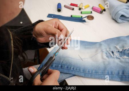 cutting a thread with scissors, seamstress workplace, jean garment repair, lifestyle and occupations, tools Stock Photo