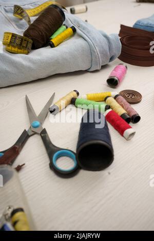 work table with colored threads, scissors, fabric and tape measure, sewing workshop with instruments, detail of objects in studio Stock Photo