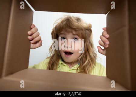 Surprised kid boy unpacking and opening carton box looking inside with surprise face. Parcel packaging or unpacking concept. Stock Photo