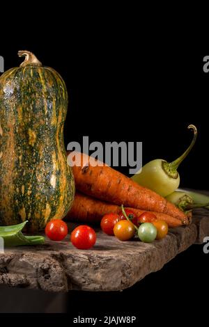 various organic vegetables on a table top, freshly harvested, homegrown pumpkin, carrot, green chili peppers and cherry tomatoes Stock Photo