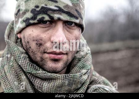 Portrait of modern combatant with dirty face, wearing a beanie hat standing in a field. Stock Photo