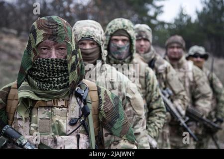 Group of skilled commandos wearing camouflage uniforms and masks, standing in line behind commander. Stock Photo