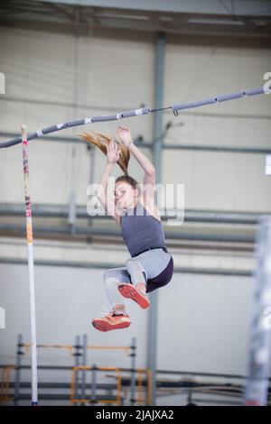 Pole vaulting indoors - young sportive woman falling down after the jump Stock Photo