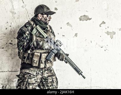 Rifleman standing near a chipped wall, with firearm in hands. Stock Photo