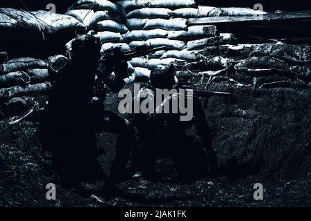 Soldiers take cover in a trench from enemy fire during a night attack. Stock Photo