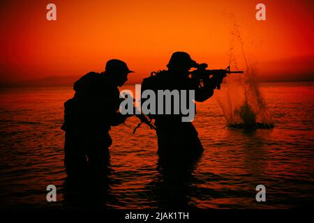 Silhouette of special forces soldiers wading through water with rifles ...