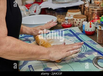 Woman rolls out the dough with rolling pin in the kitchen for making pie Stock Photo