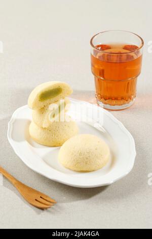 Bakpia Kukus Jogja or Bakpia Tugu, Steamed Mini Round Cake with Mung Bean Paste Inside. Servd with Tea on White Table Stock Photo