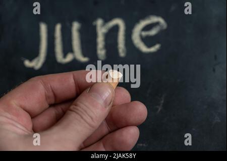 Adult male holding a piece of yellow chalk in his hand. Handwritten word JUNE on black chalkboard. Selective focus. Stock Photo