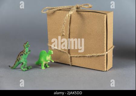 Brown cardboard box and miniatures of two dinosaurs against a gray background. Small green figures of animals of prey standing on their hind legs. Rec Stock Photo