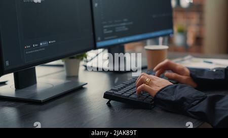 Focus on software developer hands typing source code on keyboard while looking at computer screens with programming interface. Programer sitting at desk with clipboard writing algorithm. Stock Photo