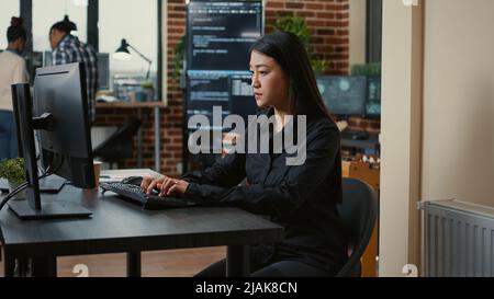 System engineer focused on writing code sitting at desk in software development office while team of coders are developing cloud computing app. Programer concentrating on creating algorithm. Stock Photo