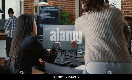 Programer pointing pencil at computer screen with software compiling code explaining source algorithm to coworker standing next to desk. Programmers discussing artificial intelligence with team. Stock Photo
