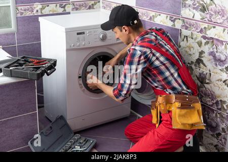 https://l450v.alamy.com/450v/2jak8p3/young-serviceman-checks-broken-washing-machine-loader-on-floor-in-room-closeup-2jak8p3.jpg