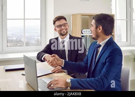 Joyful excited business male partners shake hands after successful office negotiations. Stock Photo