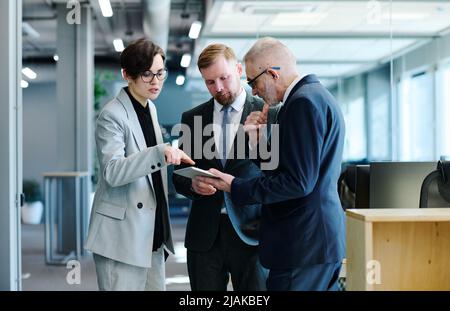 Group of business people standing at office hall and discussing online presentation on digital tablet in team Stock Photo