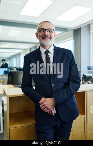 Portrait of senior successful manager in eyeglasses smiling at camera while standing at office Stock Photo